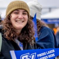 An alum smiles holding a pennant with the words "GV Proud Laker Works Here"